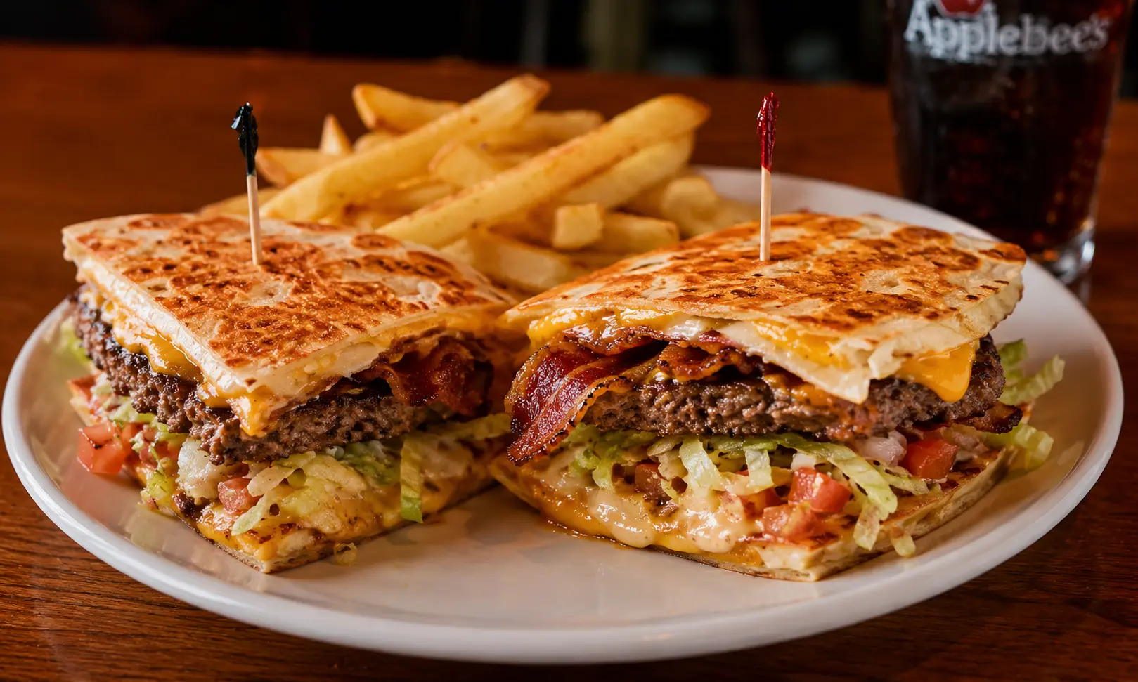 Applebee’s Quesadilla Burger served with crispy cheese quesadilla bun, seasoned beef patty, bacon, lettuce, pico de gallo, and Mexi-Ranch sauce on a restaurant plate